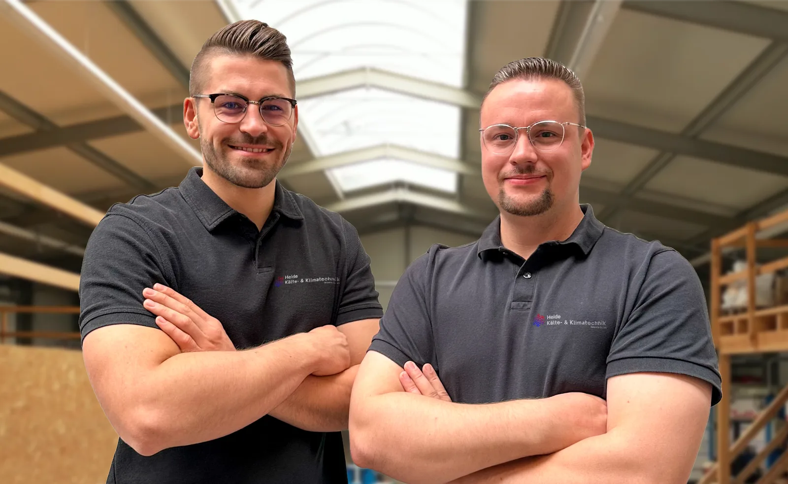 Frederik Frenzel und Tom Krause in Polohemden mit Firmenlogo in der Halle