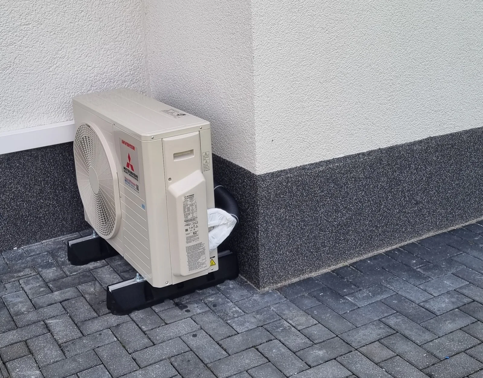 Mitsubishi-Außengerät an einer hellen Hauswand auf Pflaster