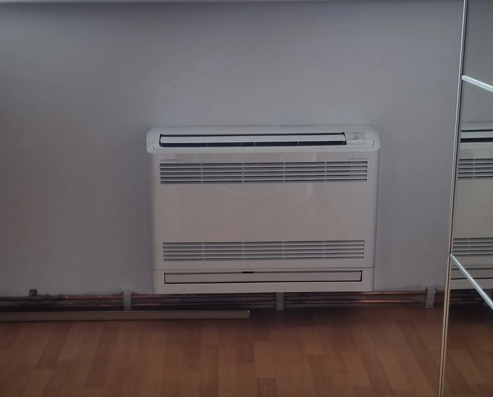 Weißes Truhengerät einer Klimaanlage an der Wand über dem Holzboden