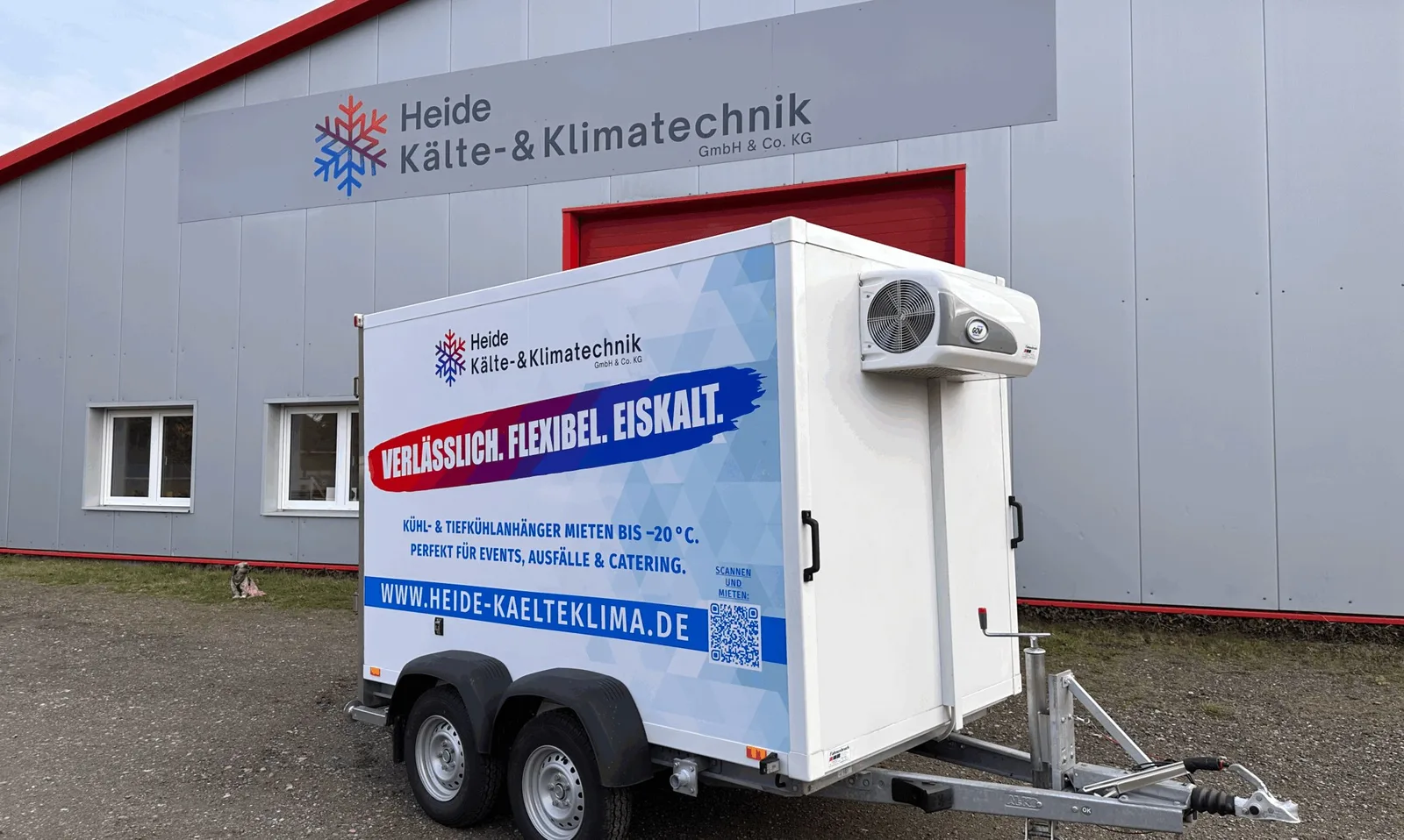 Weißer Kühlanhänger mit Firmenlogo und der Aufschrift Verlässlich. Flexibel. Eiskalt. vor der Halle mit Firmenschild