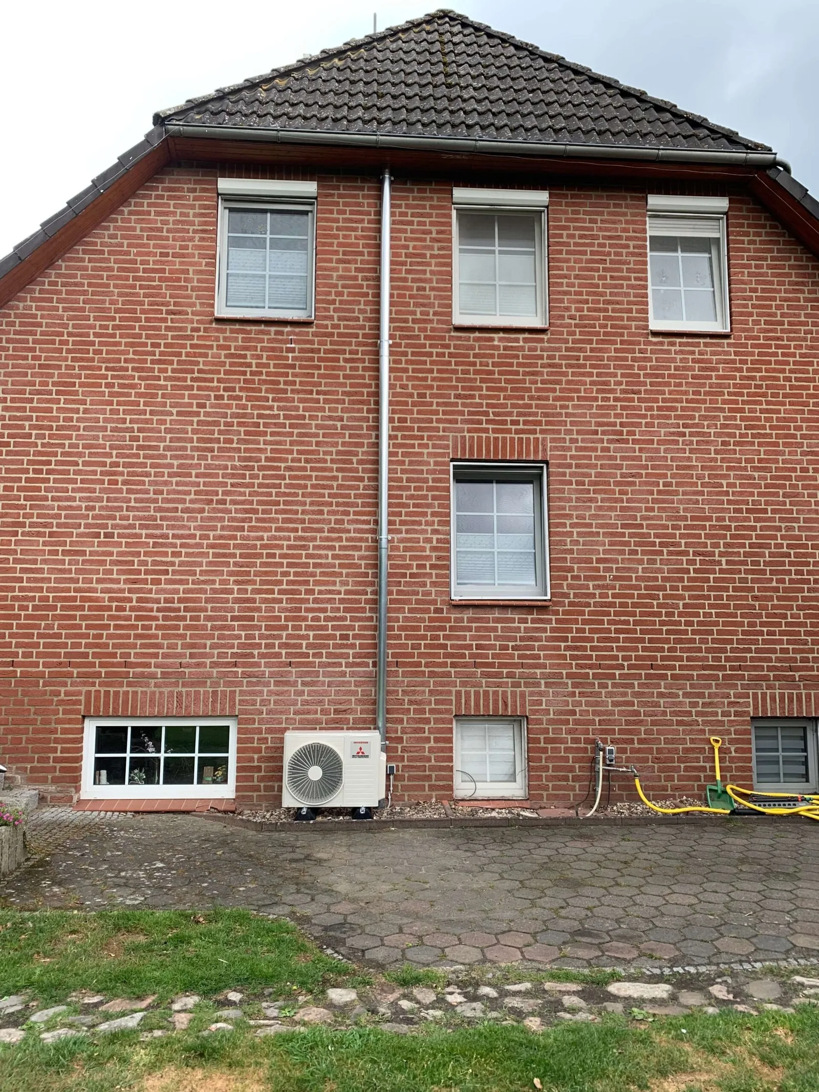 Backsteinhaus mit Außengerät und vorverlegtem Fallrohr an der Fassade